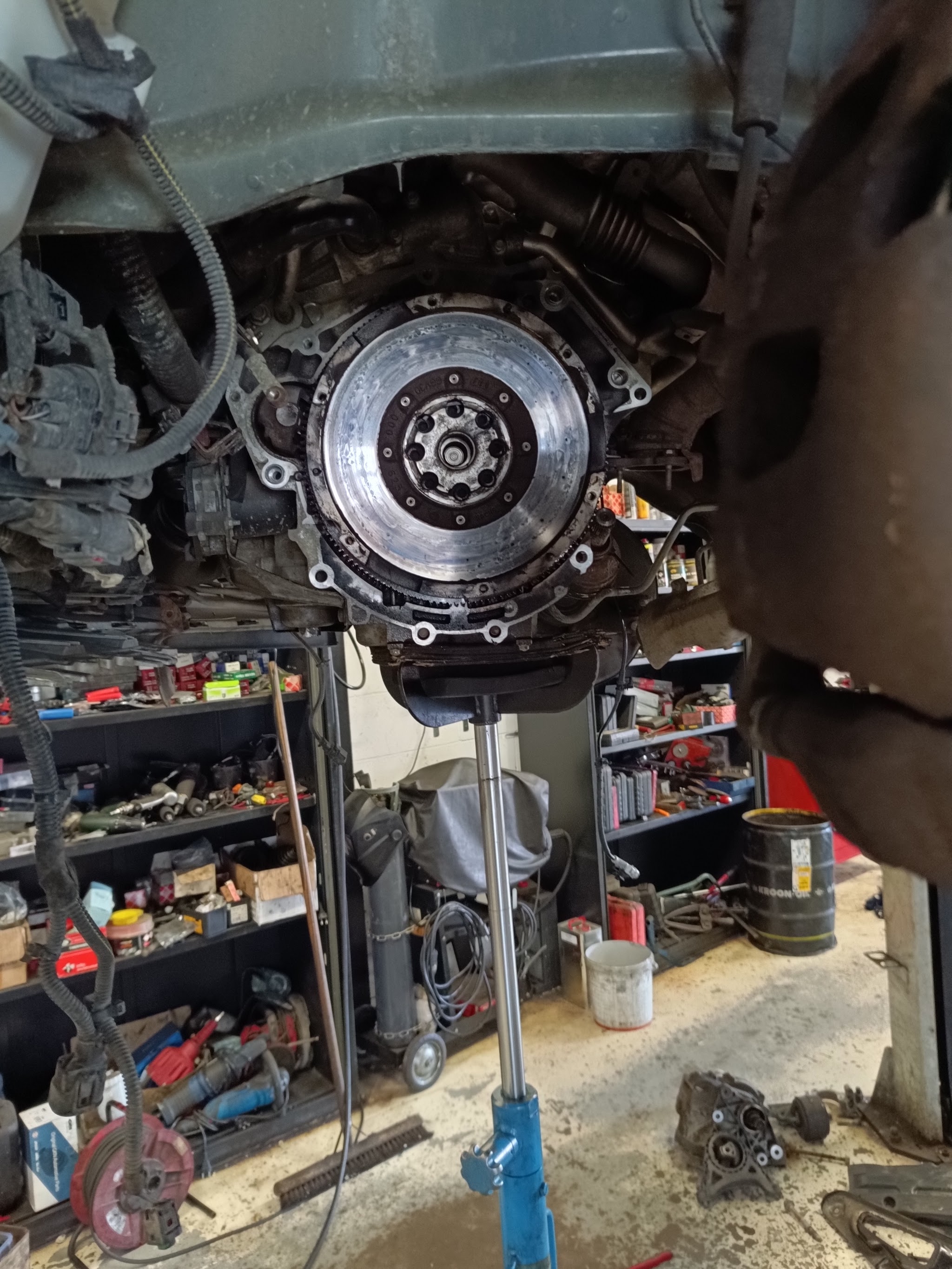 Koppeling en vliegwiel van een auto op de hefbrug, met een wand vol gereedschap en onderdelen erachter